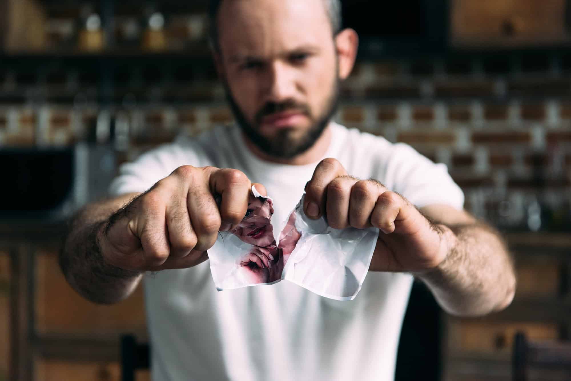 close-up shot of angry young man tearing photo of ex-girlfriend